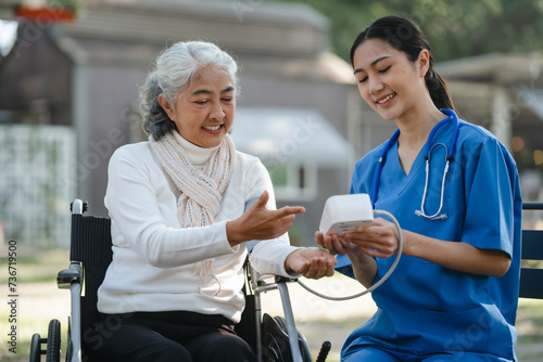 Compassionate Asian woman provides care to elderly person in wheelchair outdoors. Engaging in physical therapy, happiness, encouraging positive environment for mature individuals with grey hair.