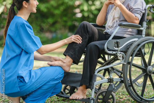Compassionate Asian woman provides care to elderly person in wheelchair outdoors. Engaging in physical therapy, happiness, encouraging positive environment for mature individuals with grey hair.