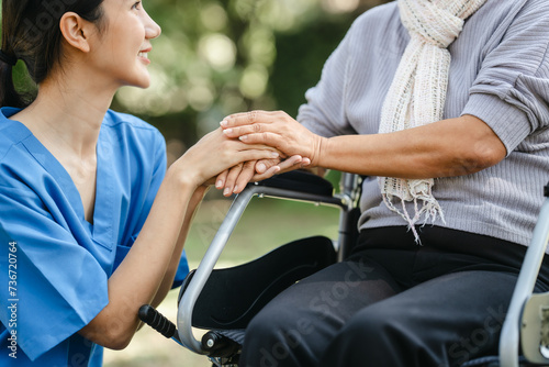 Compassionate Asian woman provides care to elderly person in wheelchair outdoors. Engaging in physical therapy, happiness, encouraging positive environment for mature individuals with grey hair.