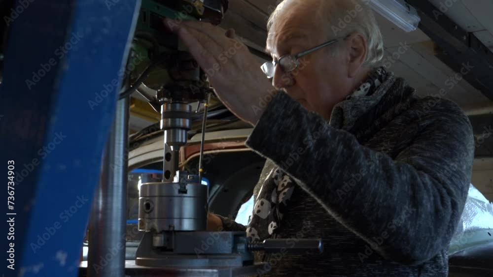 Senior metal worker operating drilling machine in a small dark workshop