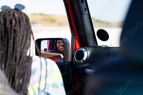 Young African American woman smiles in car side mirror on a road trip photo