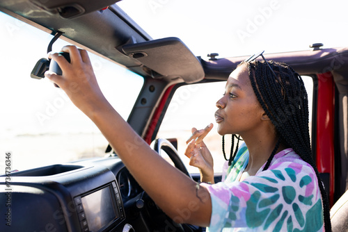 Young African American woman adjusts the rearview mirror in a car on a road trip photo