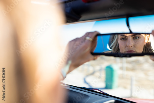 Young Caucasian woman adjusts the rearview mirror in a car on a road trip photo