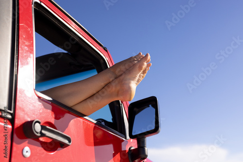 Bare feet stick out of a red car window on a road trip, with copy space photo