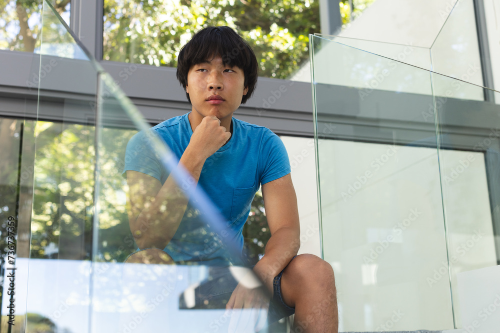 Teenage Asian boy sits sadly and thoughtfully outside a modern building Teenage Asian boy sits sadly and thoughtfully outside a modern building