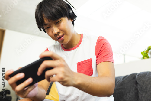 Teenage Asian boy plays a mobile game at home, fully engaged photo