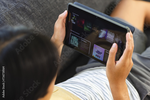 Teenage Asian boy browses a video streaming site on a tablet at home photo