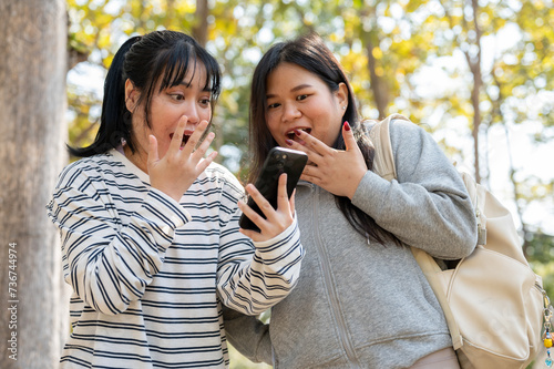 Two amazed young Asian female college students are surprised by unbelievable news on a smartphone.