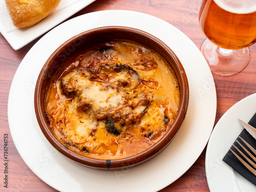 Traditional baked Balkan moussaka with aubergines, minced meat and tomato in creamy sauce served in clay bowl..