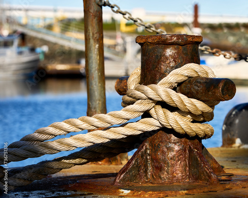 A large rope tied around a colorful rusty old cleat on a boat in an ocean marina.