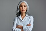Stylish confident adult 50 years old Asian female psychologist standing arms crossed looking at camera at gray background. Portrait of sophisticated grey hair woman advertising products, Generative AI