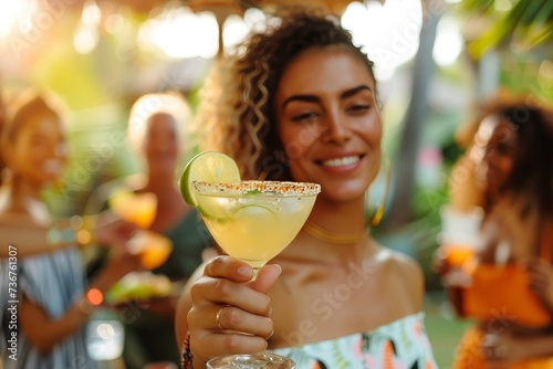 Beautiful young woman enjoying a margarita at an outdoor party with friends, feeling festive