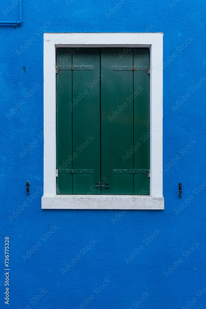 Front view of a Venetian building facade windows with wooden shutters and painted walls.