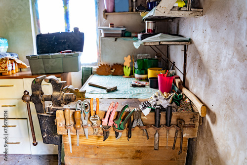 Various tools: file, screwdriver, hammer, pliers, garden tools are displayed on wooden shelf inside rustic garage or manufactory, workshop studio in a rustic garden house. Hobby, leasure activity