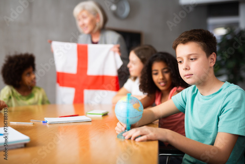 Qualified woman teacher tells pupils the history of England in lesson and holds the national flag of the country in her hands