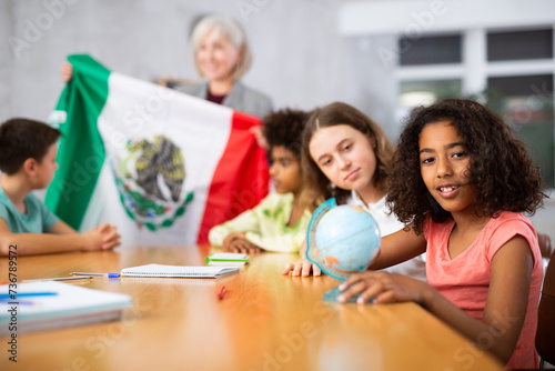 Concentrated ten-year-old schoolgirl is studying the history of Mexico in lesson and is looking for on her on the globe