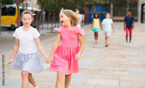 Two Caucasian girls walking and hopping together hand in hand.