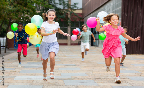 Children running through streets with balloons in hands and smiling.