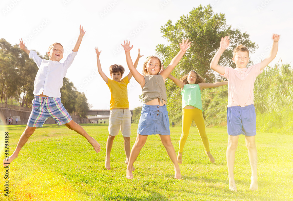 Fototapeta premium Group of children, boys and girls, jumping together on green grass in a park on sunny day
