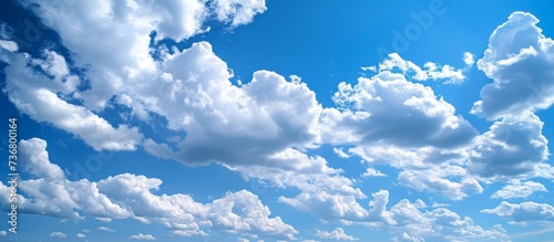 A serene natural landscape featuring an electric blue sky with fluffy white cumulus clouds, creating a calm atmosphere. The horizon is peaceful against this meteorological phenomenon