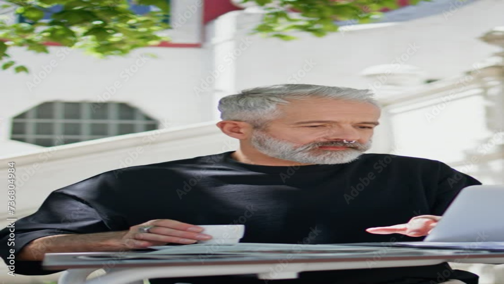 Older man browsing computer outdoors vertical. Senior working drinking coffee Older man browsing computer outdoors vertical. Senior working drinking coffee