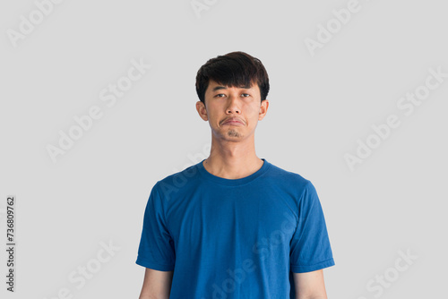 A young Asian man in his 20s wearing blue t-shirt is depressed and worried in distress standing on a gray background. Crying in anger and fear. Sad expression concept.