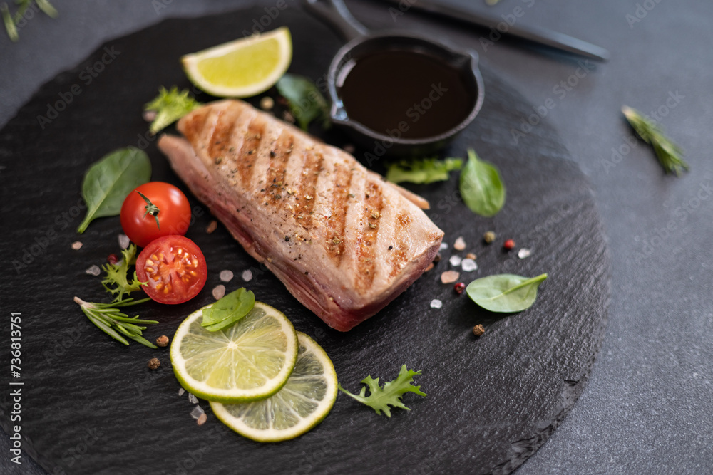 grilled cooked piece of tuna fillet on black stone serving board