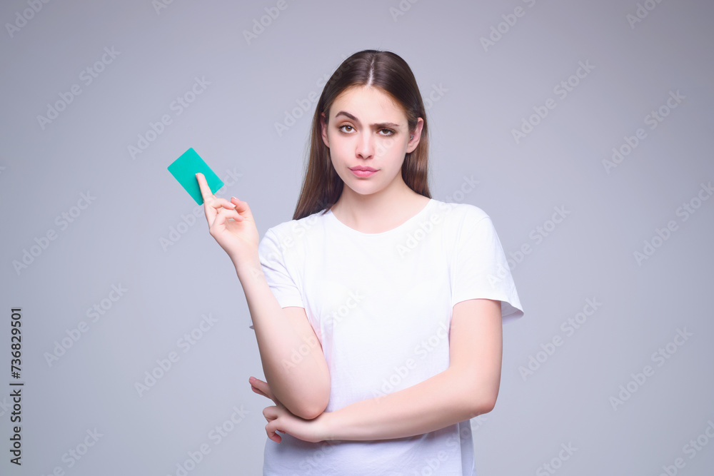 Young woman in white t-shirt holding credit card near face, isolated over gray background. Pay wit credit or debit card. Bank card. Plastic credit card. Young woman in white t-shirt holding credit card near face, isolated over gray background. Pay wit credit or debit card. Bank card. Plastic credit card.