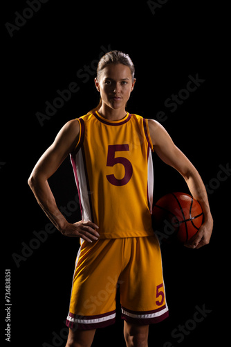 Confident female basketball player poses with a ball on a black background
