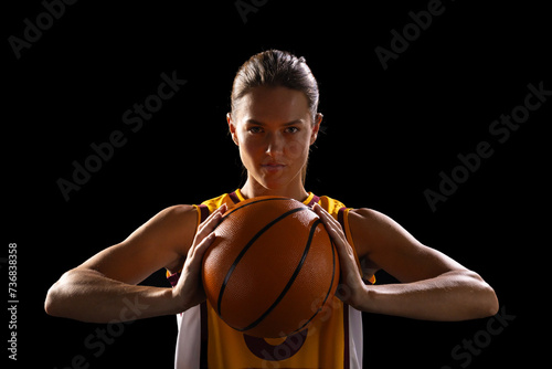 Young Caucasian female basketball player poses confidently in basketball attire on a black backgroun photo