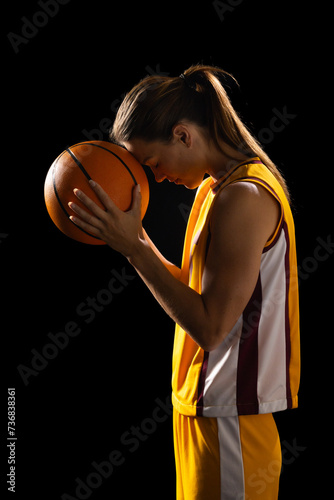 Focused young Caucasian female basketball player holds a basketball on a black background
