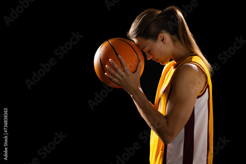 Focused young Caucasian female basketball player cradles a basketball in a studio setting on a black photo