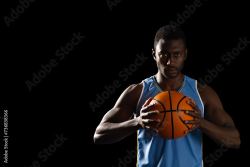 African American man holding a basketball on a black background, with copy space