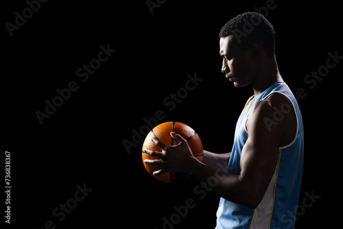 African American athlete holding a basketball on a black background, with copy space
