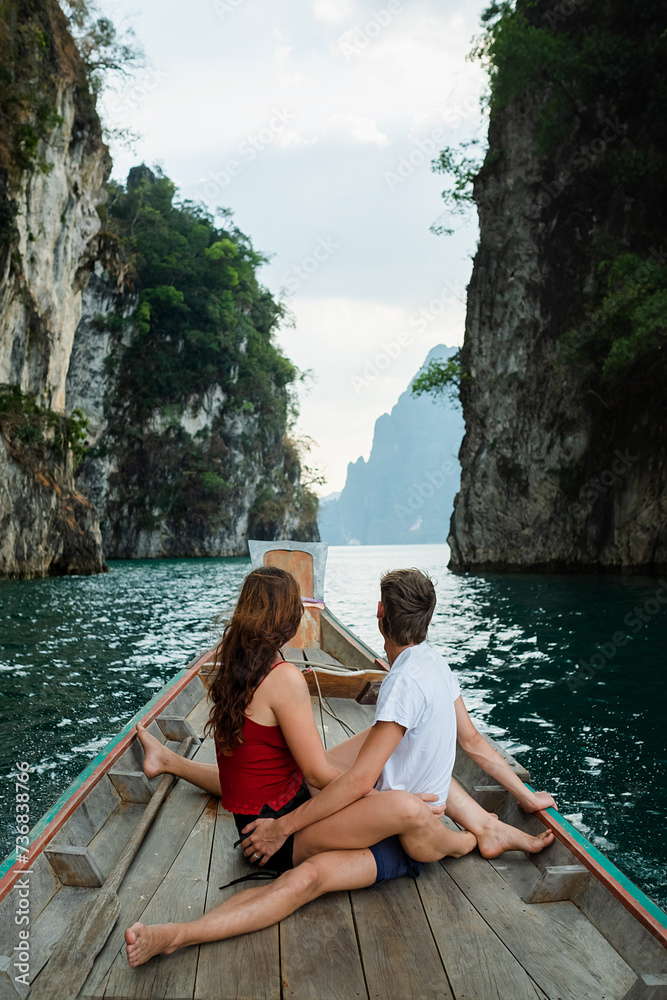 A couple of young people in love are sailing on a boat and sitting on the stern, admiring the scenery around, rear view.