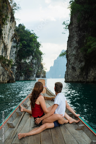 A couple of young people in love are sailing on a boat and sitting on the stern, admiring the scenery around, rear view. © Evgenii