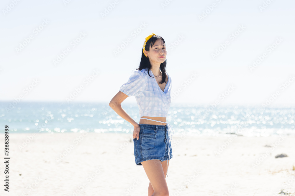 Naklejka premium Young biracial woman stands confidently on a sunny beach