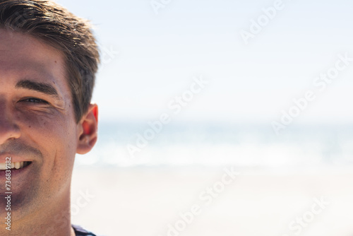 A young Caucasian man smiles brightly at the beach, with copy space unaltered