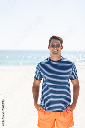 Young Caucasian man stands smiling on a sunny beach, with copy space unaltered