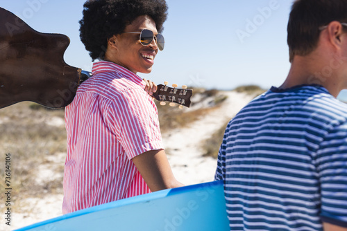 A diverse group of young friends walks to the beach, one of them, an African American man, plays gui