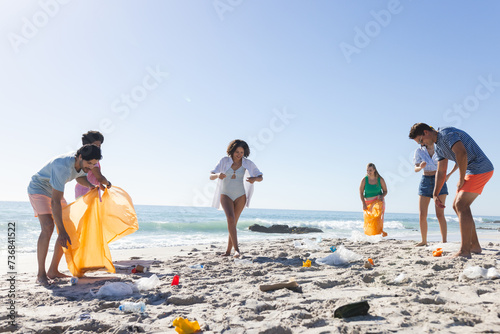 Diverse friends, part of a group, clean up a littered beach, collecting trash