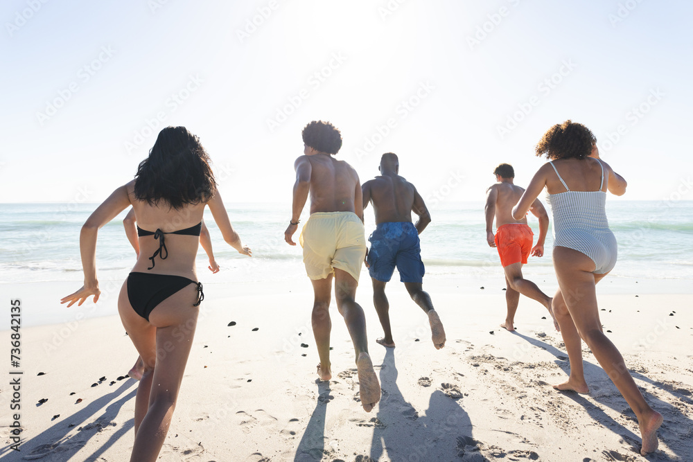 Naklejka premium Diverse friends run towards the sea on a sunny beach day