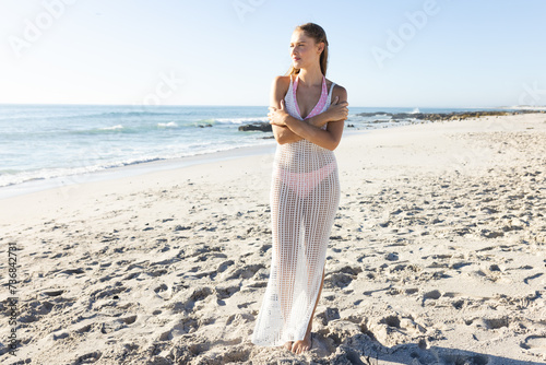 Young Caucasian woman stands on a sunny beach, with copy space