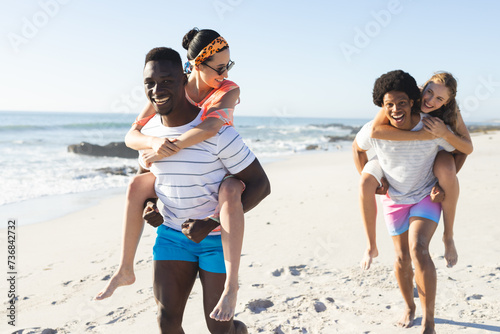 Diverse friends enjoy piggyback rides on a sunny beach