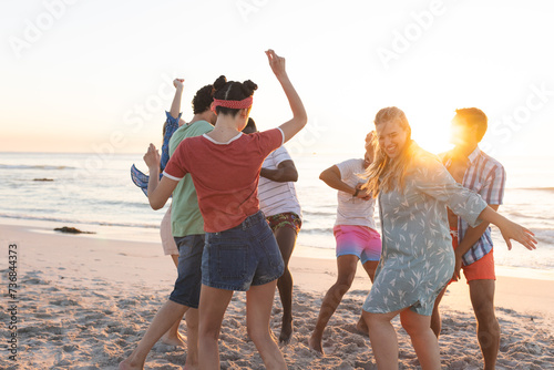 Diverse group of friends dance on the beach at sunset
