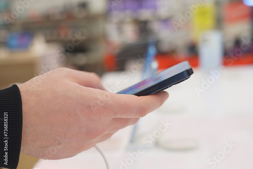 Hand of male buyer testing smartphone in electronics store