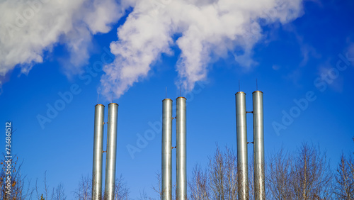 On a sunny frosty winter day, smoke is coming from the metal pipes of the city boiler house. Bright sun and blue sky.	 photo