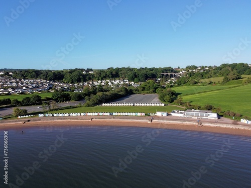 Aerial photo of Goodrington Sands Beach in Paignton Torbay showing the shoreline and a long row of beach huts with blue sea and sky on a sunny morning.