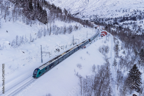 Tran on the famous Bergen - Oslo line is standing on the first track at Mjolfjell train station in the middle of the route. Snow and winter capped mountains around, also the next track is in snow.