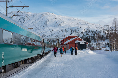Tran on the famous Bergen - Oslo line is standing on the first track at Mjolfjell train station in the middle of the route. Snow and winter capped mountains around, also the next track is in snow.